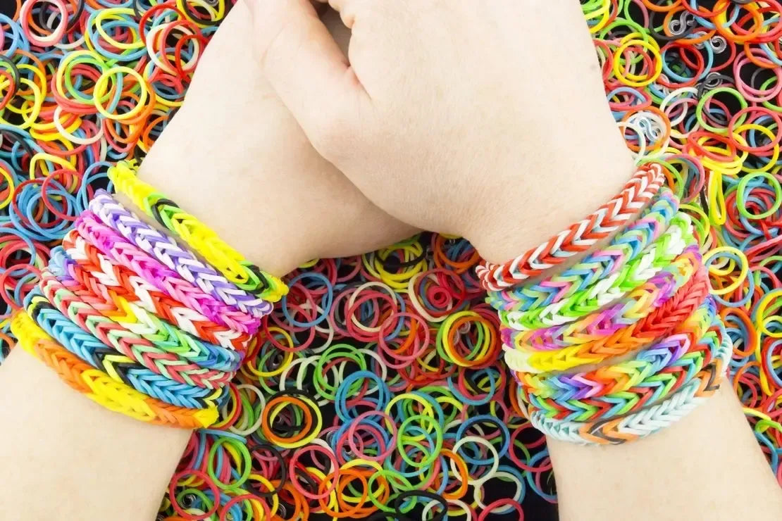 Vaizdas rodo apyrankių pynimo rinkinį Loom Bands su drugelio formos dėžute, spalvoti gumelės ir pynimo įrankiai.