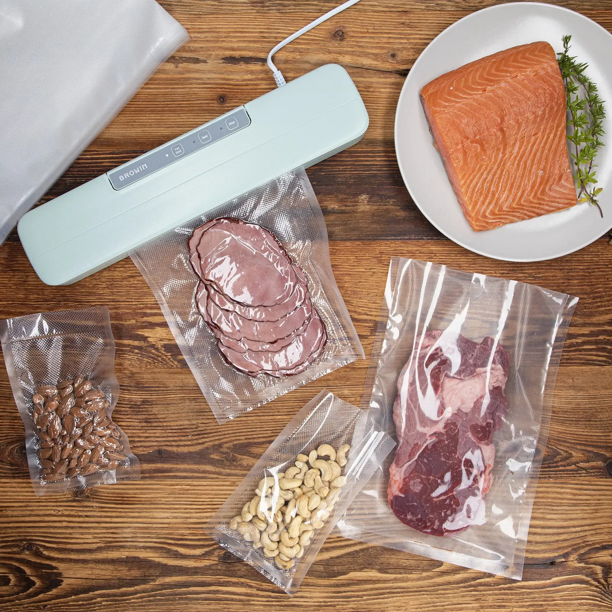 Vakuumavimo aparatas maisto produktams su rankenėlėmis ir plastiko maišelių laikikliu, juodas ir kompaktiškas, namų virtuvėje.