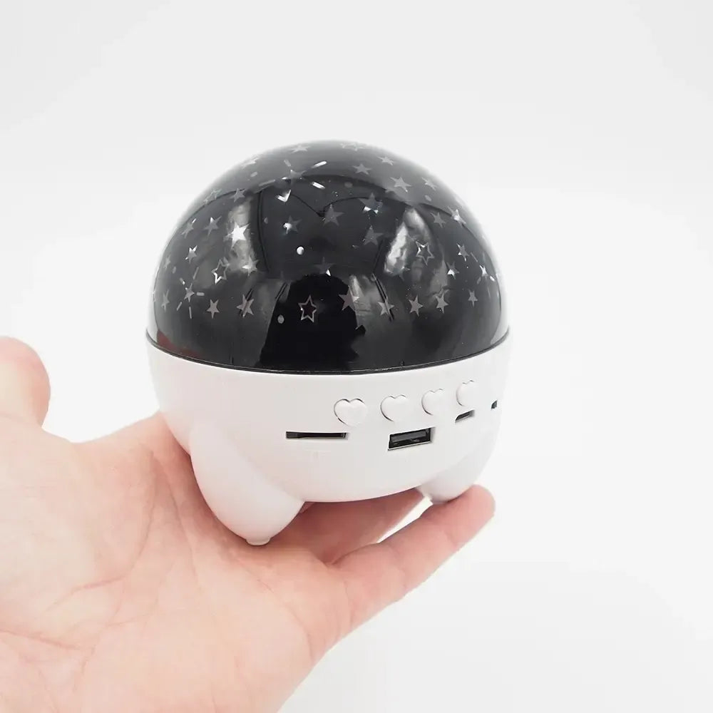 Įkraunamas žvaigždžių projektorius su Bluetooth kolonėle, rodo žvaigždžių modelius ir šviesos efektus, juodas ir kompaktiškas.